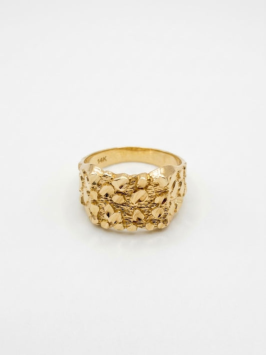 A textured gold ring with a wide, chunky band featuring a raised, organic, pebble-like pattern, photographed on a clean white background.